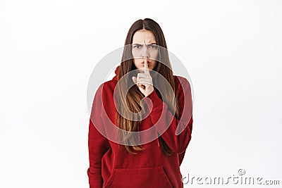 Angry bossy girl shushing, tell to be quiet, scolding loud person, press finger to lips and frowning displeased by bad Stock Photo