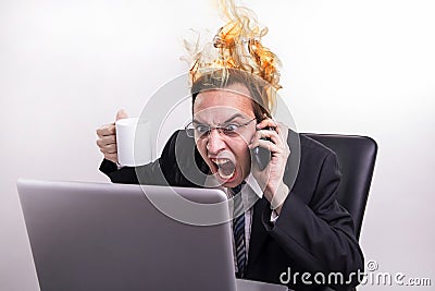 Angry business man talking on a cell phone and screaming on his laptop in the office, while his head is burning Stock Photo