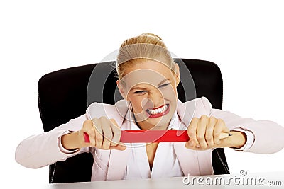 Angry business woman sitting behind the desk and trying to break huge pen Stock Photo