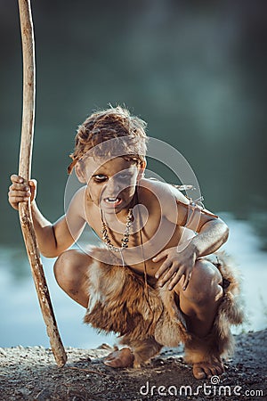 Angry caveman, manly boy with staff hunting outdoors. Ancient warrior Stock Photo