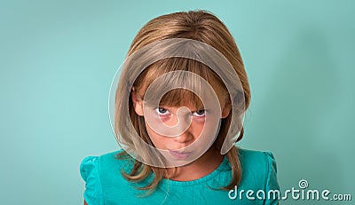 Angry child. Young girl with angry or upset expression on face on turquoise background. Negative human emotion facial expression. Stock Photo
