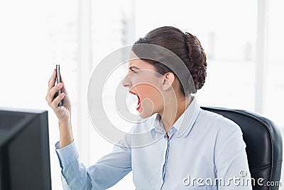 Angry classy brown haired businesswoman shouting at her mobile phone Stock Photo