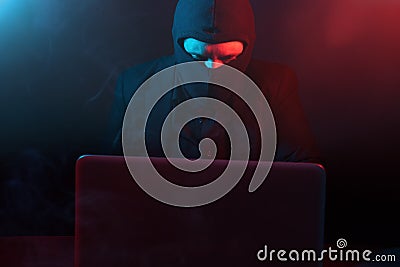 Angry computer hacker in suit stealing data from laptop illuminated by red and blue light Stock Photo
