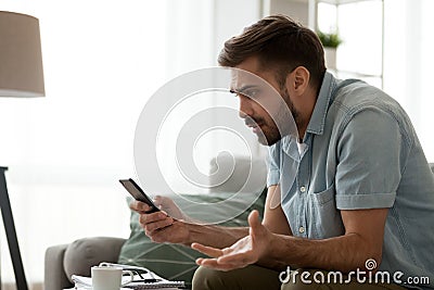 Angry confused man holding discharged phone annoyed by spam message Stock Photo