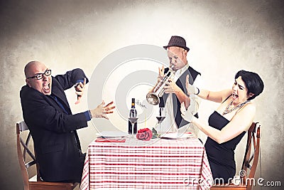 Angry couple disturbed by a trumpet musician while having dinner Stock Photo