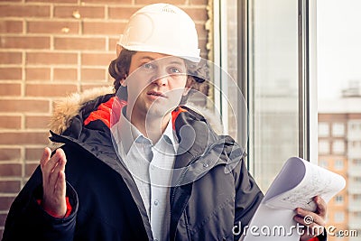 An angry disgruntled builder worker in a helmet with project drawings plans in his one hand and mobile phone in another Stock Photo