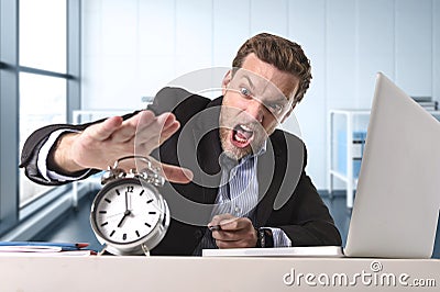 Angry exploited businessman at office desk stressed and frustrated with computer laptop and alarm clock Stock Photo