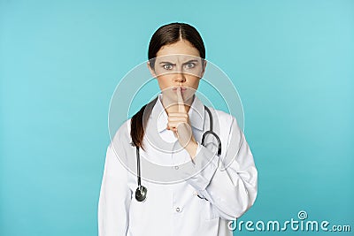 Angry female doctor, healthcare medical worker shushing with disapproval, taboo quiet gesture, silence someone, standing Stock Photo
