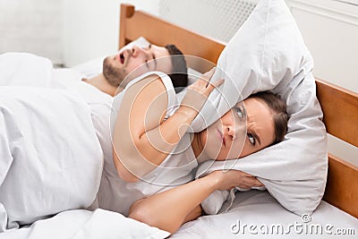 Angry Girlfriend Covering Ears Lying Near Snoring Boyfriend In Bed Stock Photo