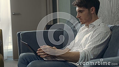 Angry guy hitting laptop indoors. Wicked man working on computer in hotel room. Stock Photo