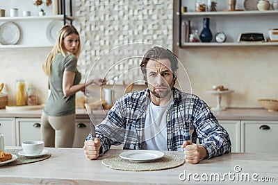 Angry hungry dissatisfied millennial caucasian man with stubble ignoring woman and wait for food in kitchen Stock Photo