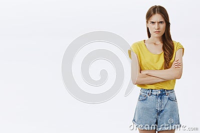 Angry insulted pressured attractive girl in yellow t-shirt and shorts holding hands crossed on chest frowning from anger Stock Photo