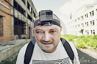 Angry man with action camera on head looking at camera and go. Portrait of travel blogger in urban background Stock Photo