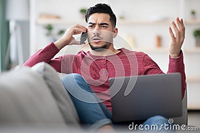 Angry man with notebook on his lap having phone conversation Stock Photo