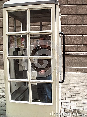 Angry man standing in a white telephone booth and screaming into the phone Stock Photo