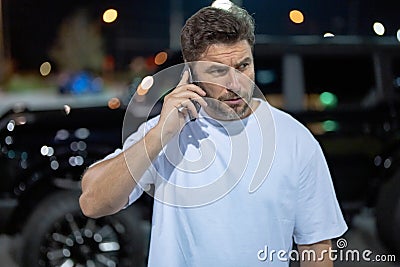 Angry man talking on phone on night urban street. Dangerous aggressive man talking on phone with serious face. Criminal Stock Photo