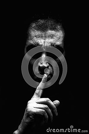 Angry mature man with an aggressive look making the silence sign in a threatening and creepy way Stock Photo