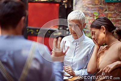 Angry mother in law looking reproachfully her son-in-law who is justifying. her daughter sitting beside with her hand on a face, Stock Photo