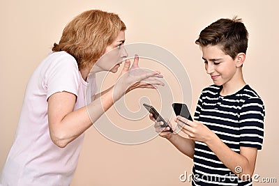 Angry mother scolding her smiling son with two smartphones Stock Photo