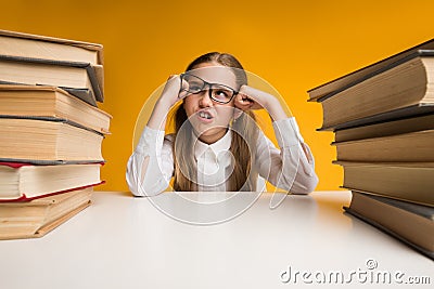 Angry Schoolgirl Sitting Among Books Tired Of Homework, Yellow Background Stock Photo