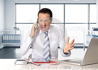 Angry senior businessman in stress working and talking on mobile phone at computer desk Stock Photo