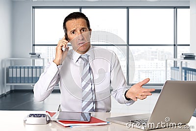 Angry senior businessman in stress working and talking on mobile phone at computer desk Stock Photo