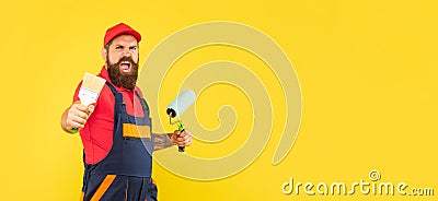 angry shouting bearded man renovator in work clothes hold paint roller and brush Stock Photo