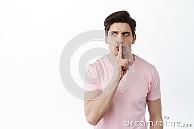 Angry suspicious man looks aside and shushing, tell to shut up, be quiet, need silence, show taboo gesture, standing Stock Photo