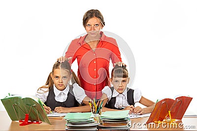 Angry teacher stands behind students sitting at her desk and puts her hands on the heads of children Stock Photo