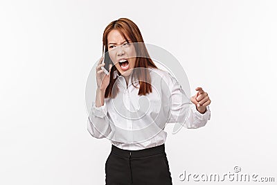 Angry and tensed, aggressive young asian woman cursing as talking on phone, clench fist outraged screaming in mobile Stock Photo