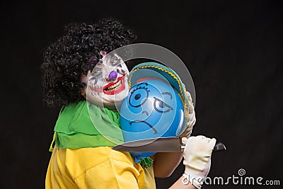 Angry ugly clown wants to kill a balloon in the cap Stock Photo