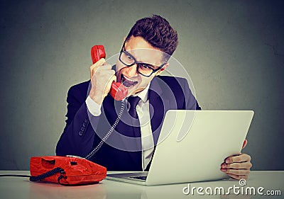 Angry young business man calling customer service with a laptop failure screaming on the phone Stock Photo