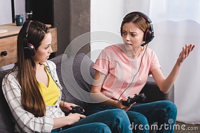 angry young woman in headphones with joystick in hand quarreling with female friend Stock Photo