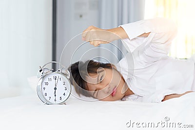 Angry young woman looking at alarm clock with clench one`s hand Stock Photo