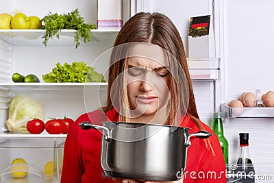 Angy displeased female housewife looks in pot with foul meal, sm Stock Photo