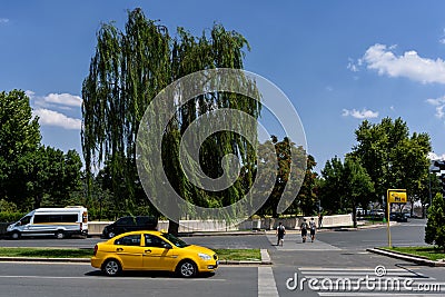Ankara, Turkey - June 24, 2018: Yellow taxi stands near a beautiful spreading tree near the entrance to the tomb of Editorial Stock Photo