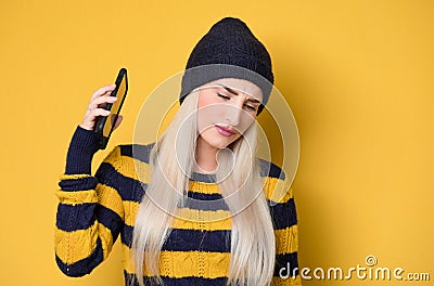 Annoyed girl on the phone, model wearing woolen cap and sweater, isolated on yellow background. Annoying woman talking. Nuisance Stock Photo