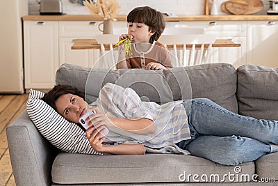 Annoyed young mom rolling eyes tired of loud little kid. Tired young mother try to relax after work Stock Photo