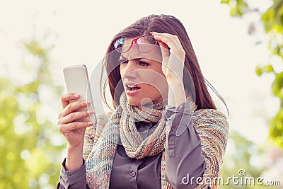 Annoyed upset woman in glasses looking at her smart phone with frustration while walking on a street Stock Photo