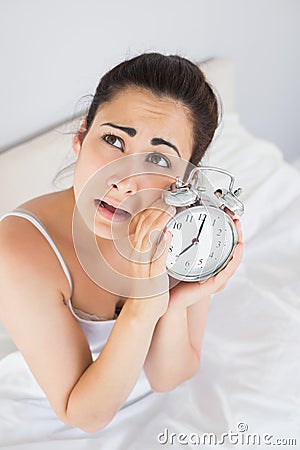Annoyed woman holding an alarm clock in bed Stock Photo