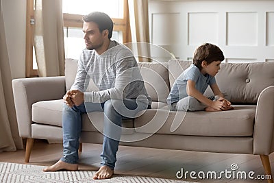 Annoyed young father sitting back to back with little son. Stock Photo