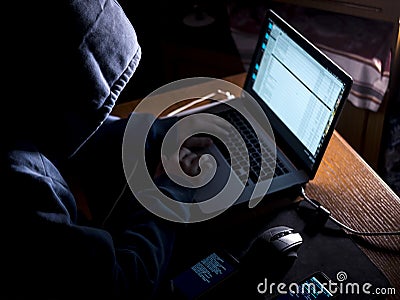 Anonimous man in the hoodie in dark studio typing text online on internet with copy space Stock Photo