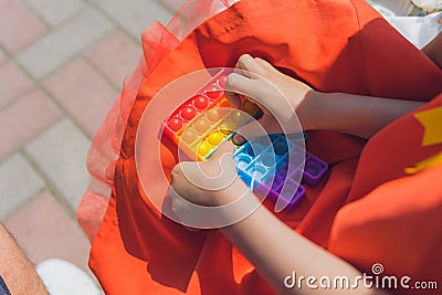 Anonymous child hold in his hands sensory toy pop it and shows it in front of himself.Rainbow color.Antistress toy for Stock Photo