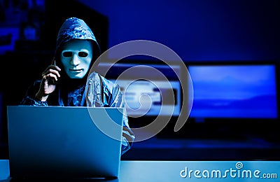 Anonymous computer hacker in white mask and hoodie.Obscured dark face using laptop computer for cyber attack and calling Stock Photo