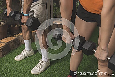 An anonymous couple does dumbbell Romanian deadlifts on the artificial grass mat of a home gym. Closeup shot Stock Photo