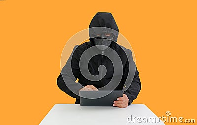 Anonymous hooded hackers hacking data of tablet on orange background. Image with Clipping path Stock Photo