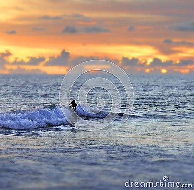 Anonymous silhouette of male or female surfer surfing and riding waves on sunset wild sea under a stunning orange sky in beauty ho Stock Photo