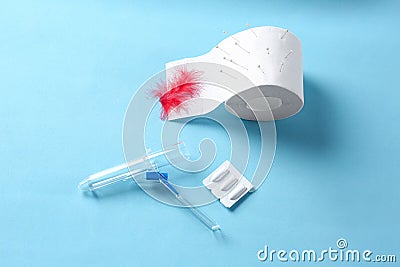 Anoscope, suppositories and toilet paper with red feather on light blue background. Hemorrhoid treatment Stock Photo