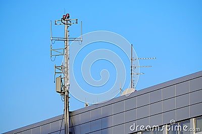 An antenna with multiple transmitters and receivers mounted on the roof of an office building has flashing red beacons Stock Photo
