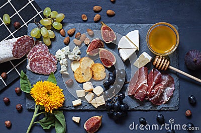 Antipasti food dark blue flat lay with nuts, honey, cured meat, salami, cheeses, grapes and figs. Stock Photo